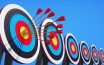 Row of archery targets with hits by several arrows with sun against a clear blue sky
